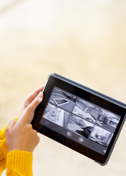 Hands of caucasian woman holding tablet and pointing to security camera views on screen, copy space. Technology, security, convenience and domestic life. Hands of caucasian woman holding tablet and pointing to security camera views on screen, copy space. Technology, security, convenience and domestic life.